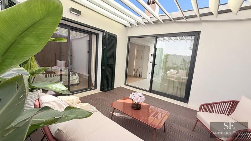 Outdoor patio with white pergola, wooden deck, terracotta-colored furniture, and tropical plants.