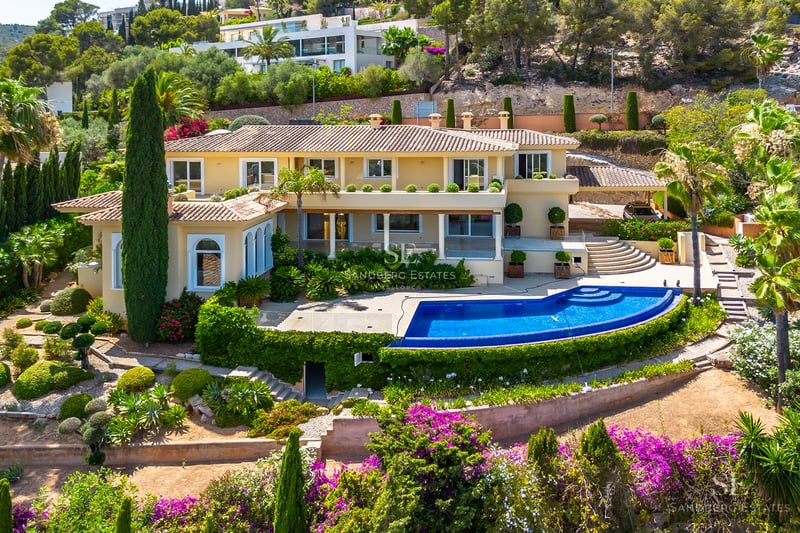 View of a luxury infinity pool with sun loungers and umbrellas, surrounded by a garden and overlooking the sea. Modern and elegant architecture.