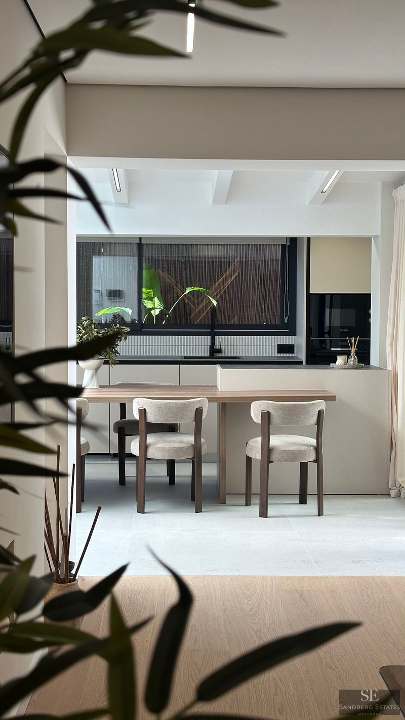 Modern kitchen featuring a light wood dining table attached to a beige island, with stylish chairs and a large window.