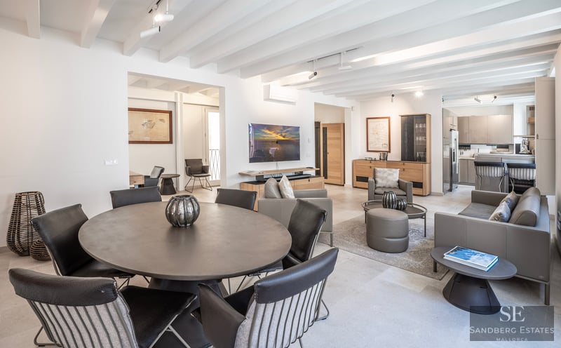 Salon moderne avec table ronde, canapés en cuir, plafond à poutres blanches et télévision murale.