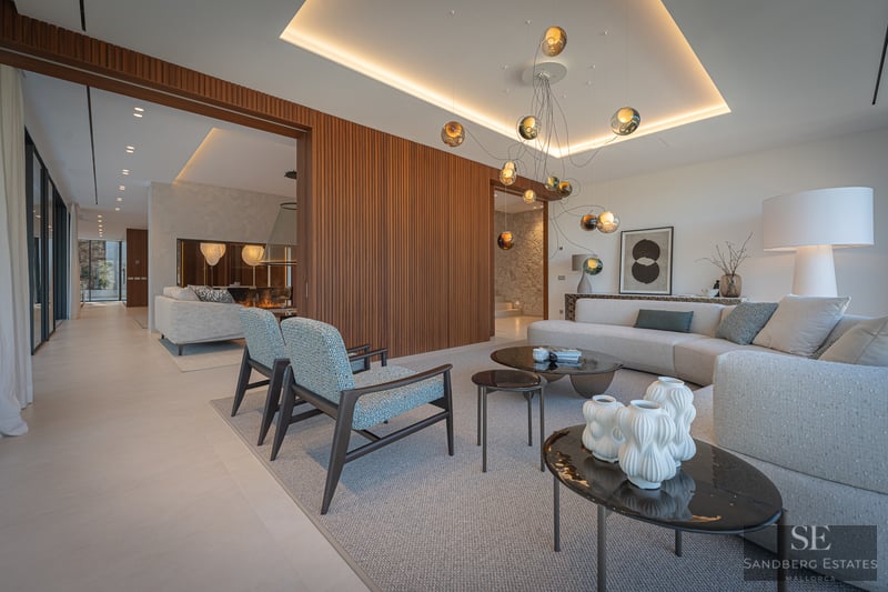 Modern living room with a large gray sofa, blue armchairs, wood slatted wall, and a unique glass orb chandelier.