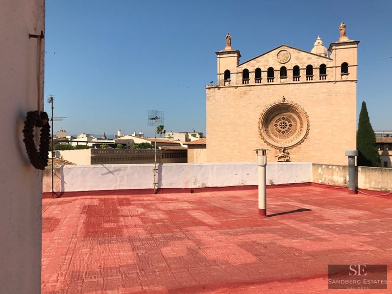 Red tiled rooftop overlooking a stone church facade with a rose window under a clear blue sky.