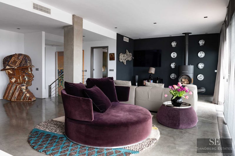 Salón moderno con sofá circular de terciopelo ciruela, suelos de hormigón pulido y pared de acento negra con chimenea.