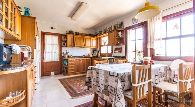 Cocina luminosa de estilo rústico con armarios de madera, mesa de comedor con mantel y luz natural.