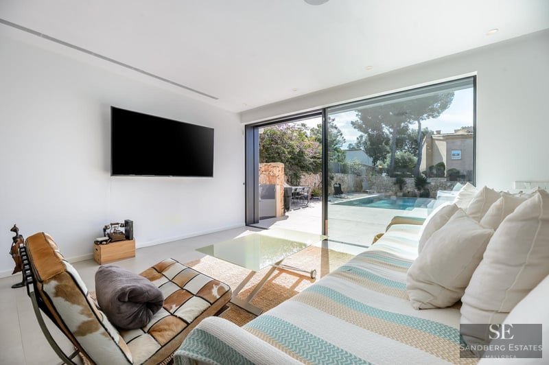Bright living room with a striped sofa, large TV, and floor-to-ceiling glass doors leading to a pool terrace.