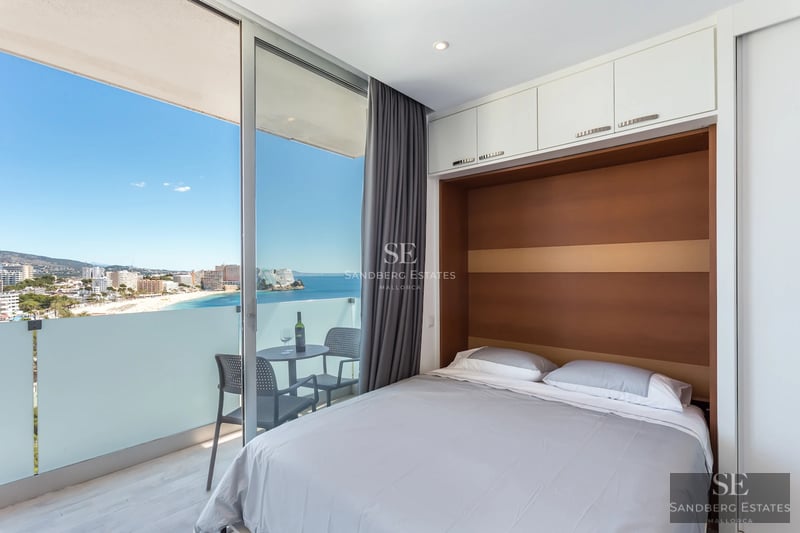 Amplio balcón con vistas al mar. Diseño moderno, barandilla de cristal y suelo de madera. Espacio luminoso y abierto.