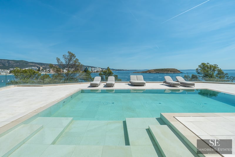 A turquoise swimming pool on a stone terrace with sun loungers overlooking the Mediterranean sea and a distant island.