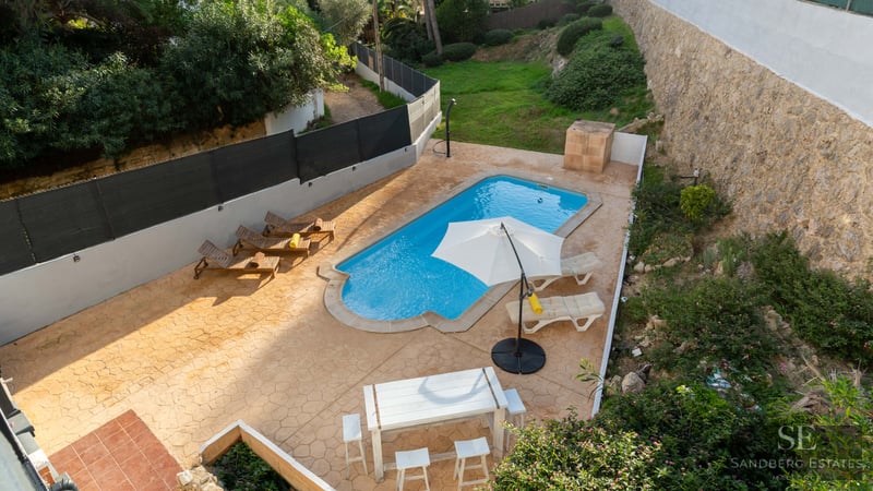 Vue aérienne d'une piscine turquoise entourée d'une terrasse en terre cuite avec transats et coin repas.