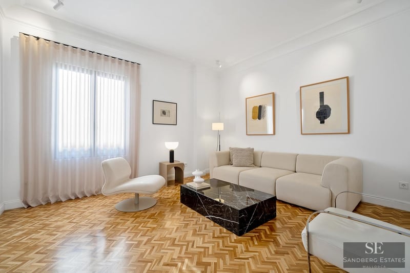 Bright living room with white walls, herringbone wood floors, a beige sofa, and a black marble coffee table.
