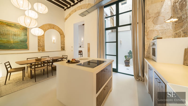 Modern kitchen featuring an island, wooden dining set, paper globe pendants, and exposed historic stone arches.