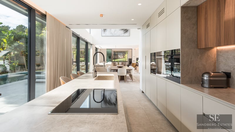 Cuisine moderne avec un grand îlot en pierre, des appareils intégrés et des baies vitrées donnant sur une piscine.