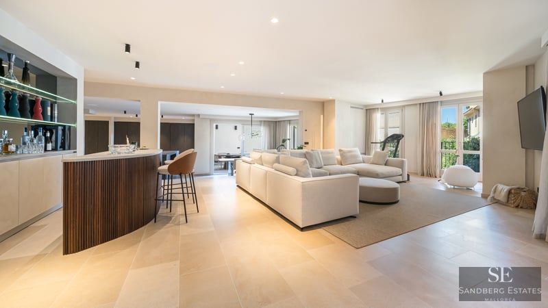 Spacious modern living room with a large white sofa, wooden bar counter, and natural stone flooring.