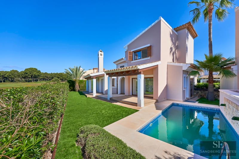 Modern Mediterranean villa featuring a private swimming pool, lush green lawn, and palm trees under a clear blue sky.