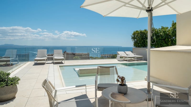 Spacious balcony with panoramic sea views. Glass railing, wooden floor, modern outdoor furniture. Soft lighting and relaxing atmosphere.