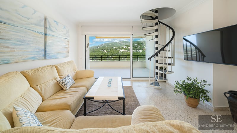 Bright living room featuring a cream sofa, black and white spiral staircase, and balcony with mountain views.