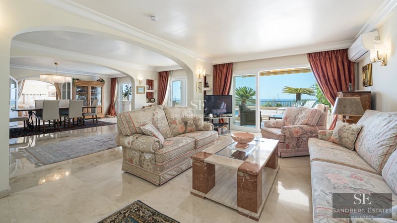 Spacious living room with large windows, light wood floors, and garden view. Modern gray sofa and minimalist decor.