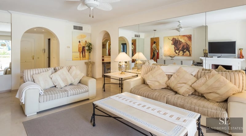 Spacious, bright living room with large windows, light wood flooring and modern furniture. Panoramic outdoor views.