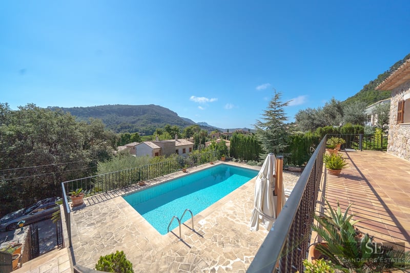 Rectangular swimming pool surrounded by a stone terrace with panoramic mountain views under a clear blue sky.