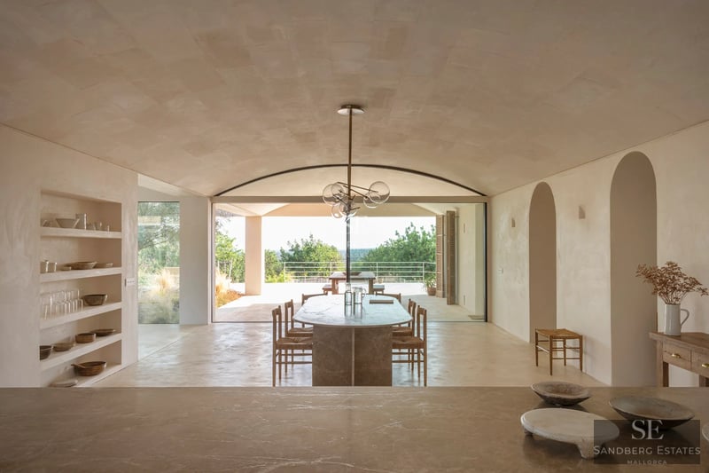 Amplia piscina con tumbonas, sombrillas y exuberante vegetación. Casa moderna al fondo con grandes ventanales y balcón.