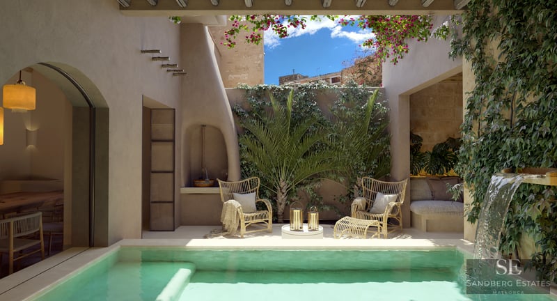 Sunlit courtyard with turquoise plunge pool, waterfall, wicker chairs, and lush greenery under a blue sky.