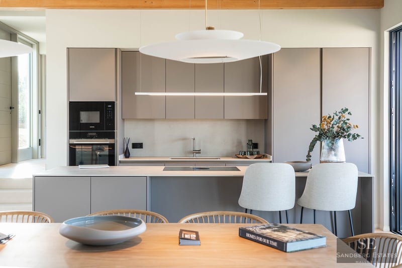A contemporary kitchen featuring taupe handleless cabinets, a central island with stools, and elegant pendant lights.