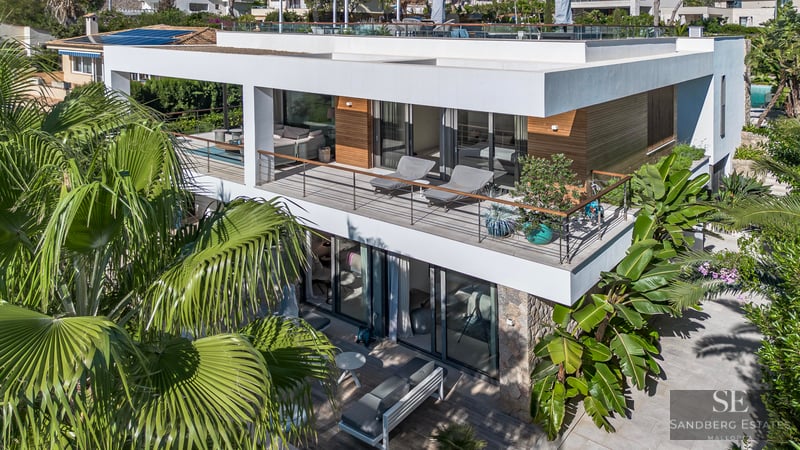 Vue aérienne d'une villa moderne blanche de deux étages avec balcons en verre et palmiers tropicaux.