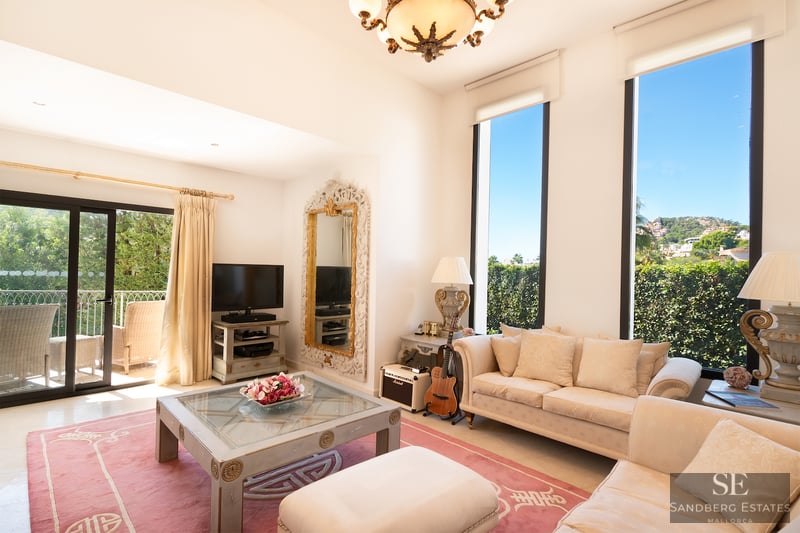 Bright living room with cream sofas, a pink rug, large vertical windows, and a sliding door leading to a balcony.