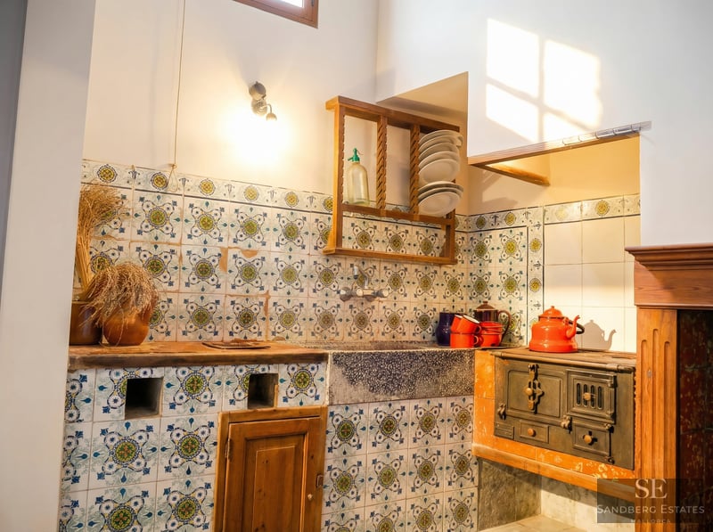 Rustic kitchen featuring hand-painted patterned tiles, a stone sink, and a vintage cast iron wood-burning stove.