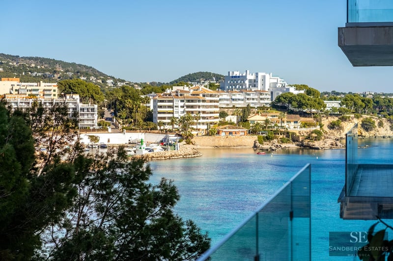 High-angle view of a turquoise bay with white buildings and a marina seen through a glass balcony railing.