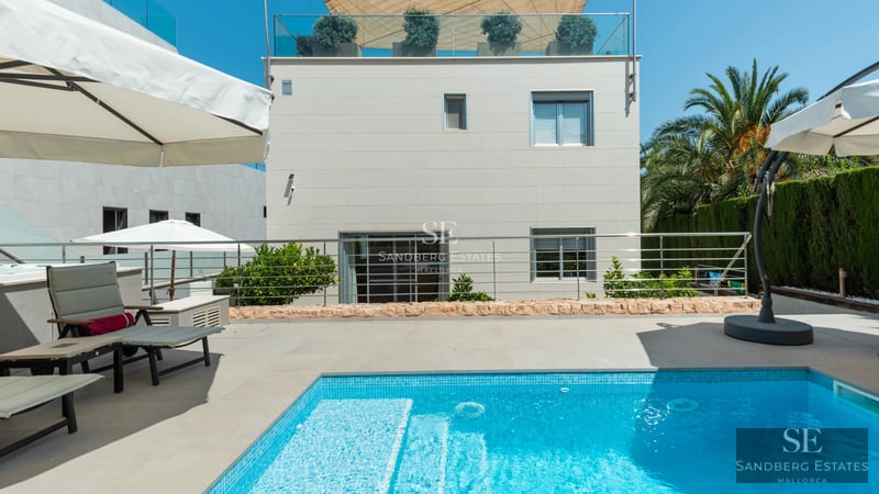 Exterior view of a luxury residence featuring an infinity pool, expansive windows, and modern landscaping.