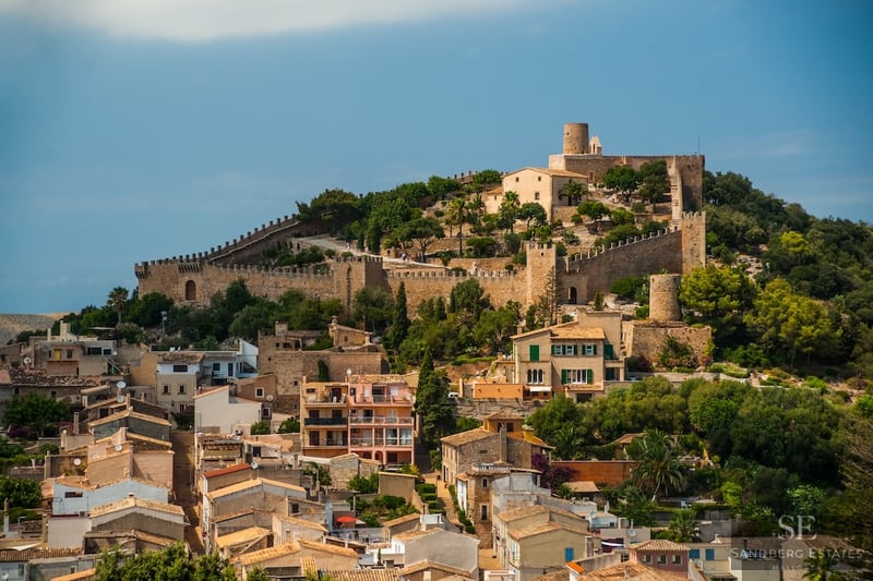 Mediterranean hillside village crowned by a medieval fortress with stone walls under a clear blue sky.