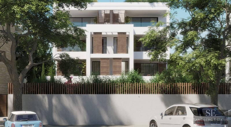 Weißes vierstöckiges modernes Gebäude mit Holzläden und Glasbalkonen, umrahmt von großen grünen Bäumen.