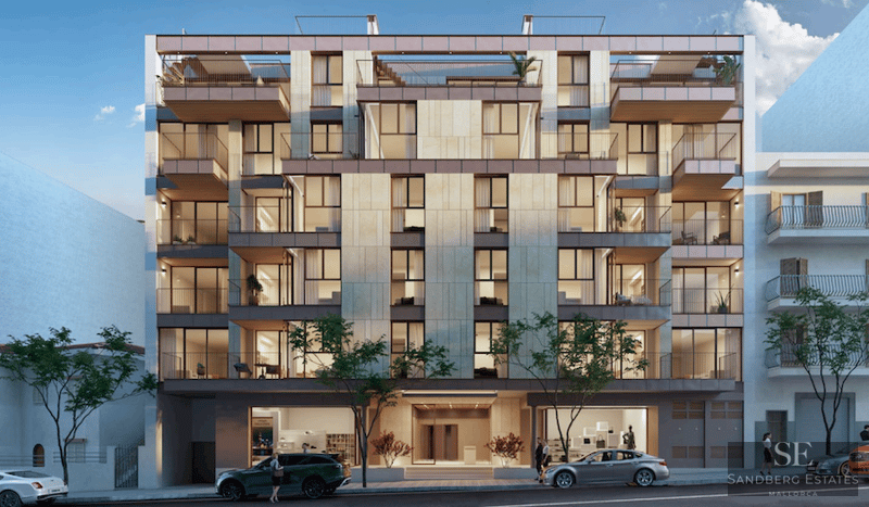 Front view of a contemporary six-story apartment building with beige stone cladding, large windows, and balconies.