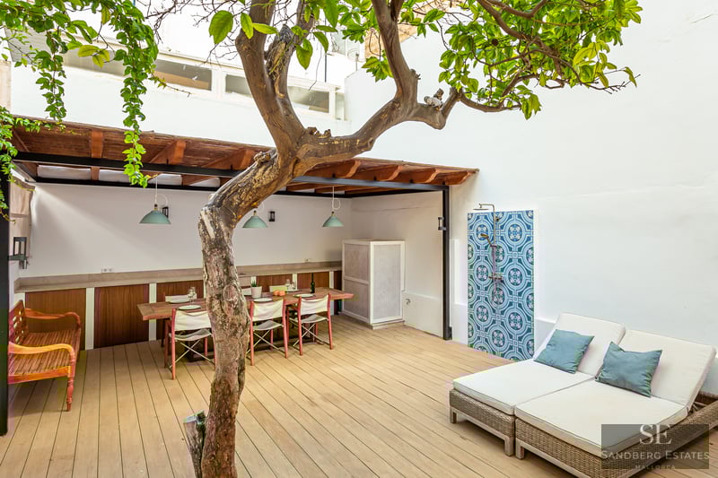 Wooden deck terrace featuring a dining table under a pergola, a large sunbed, and an outdoor shower with blue tiles.
