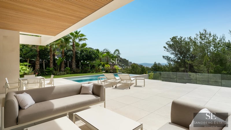 Panoramic view of modern villa with infinity pool and expansive terraces. Sleek and minimalist architecture. Blue sky and lush vegetation.