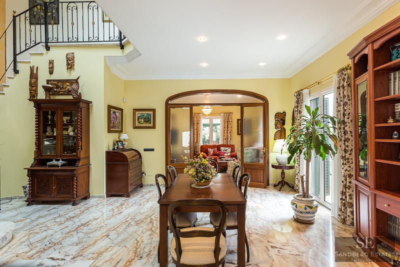 Spacious dining room featuring veined marble floors, classic wooden furniture, and African art decor.