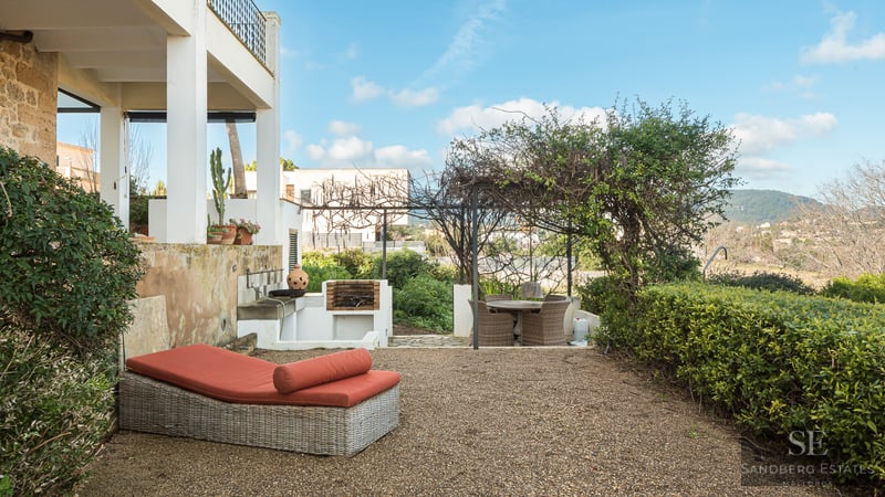 Outdoor terrace featuring a wicker sunbed with orange cushions, a built-in stone grill, and a pergola-shaded dining area.