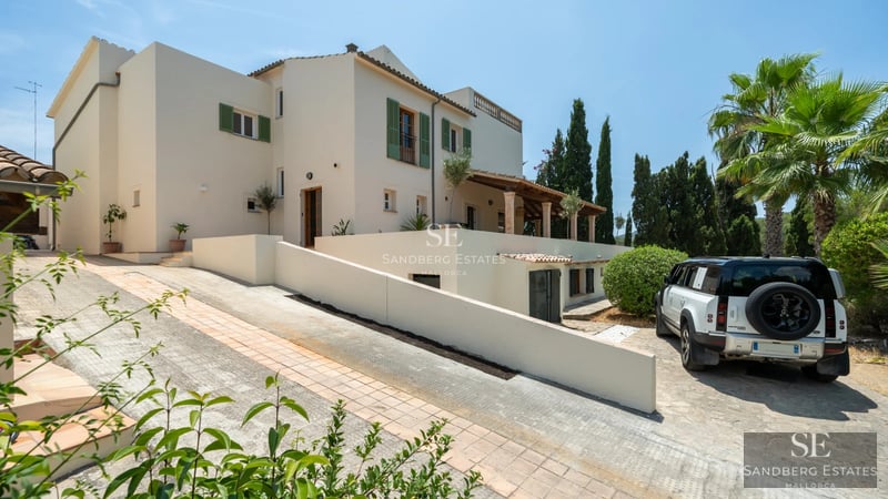 Vista de una piscina moderna con tumbonas elegantes, rodeada de un jardín verde y una casa minimalista de dos pisos.