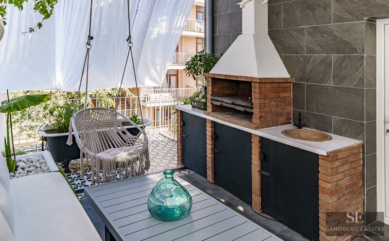 Elegant Outdoor Terrace with Built-in Barbecue A modern terrace featuring a brick barbecue, a hanging macrame chair, a dining table, and decorative tiling.