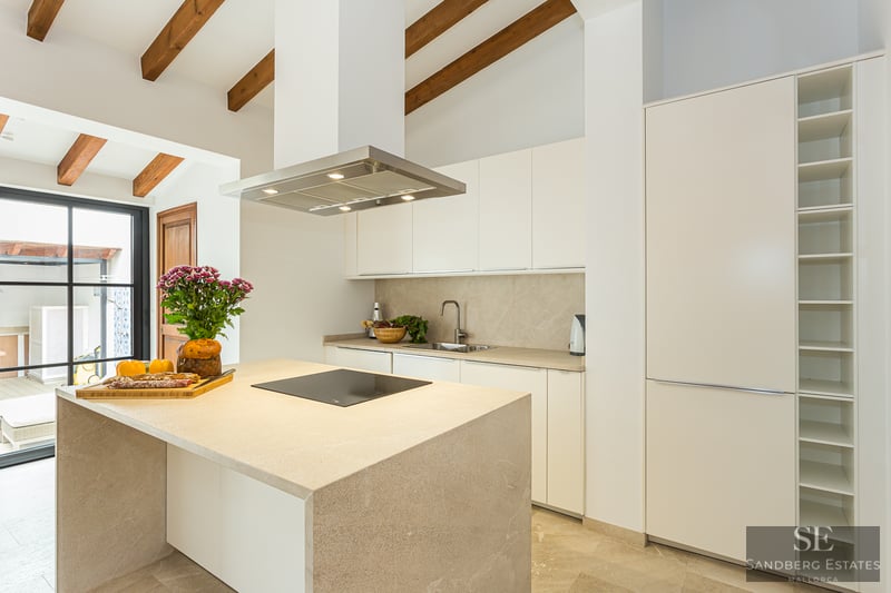 Bright kitchen featuring a stone island, exposed wooden ceiling beams, and minimalist white cabinetry.