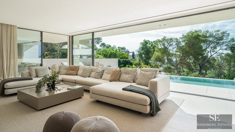A bright, modern living room with a large cream sectional sofa looking out through glass walls to a private pool and trees.