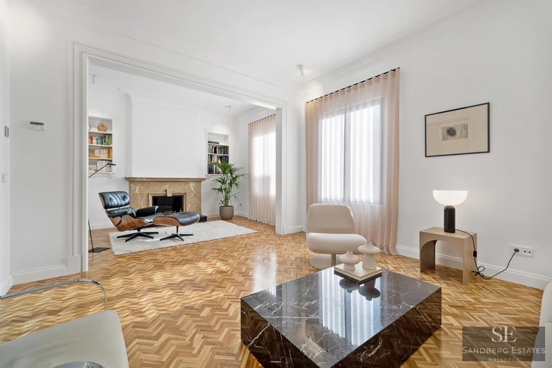 Bright living room featuring herringbone wood floors, a black marble coffee table, and an Eames lounge chair by a fireplace.