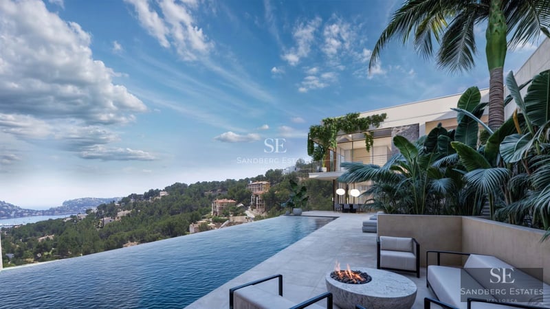 View of an infinity pool with sun loungers and a modern villa featuring large windows. Lush vegetation and clear sky.