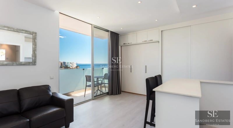 Amplio salón con ventanales, suelos de madera clara, y decoración minimalista. Iluminación natural destacando texturas suaves y colores neutros.