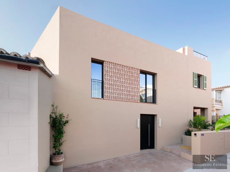 Façade beige avec porte noire, fenêtres à balustrades et écran décoratif en terre cuite.