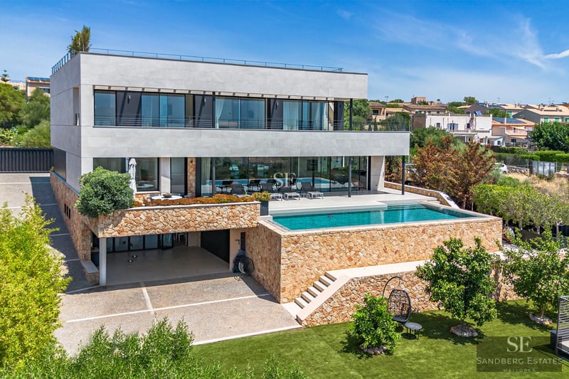 Spacious, bright living room with large windows, light wood floor, and modern furniture. Garden view with pool.