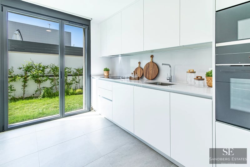 View of a luxurious pool with sun loungers and umbrellas, surrounded by greenery and a modern house with large windows.