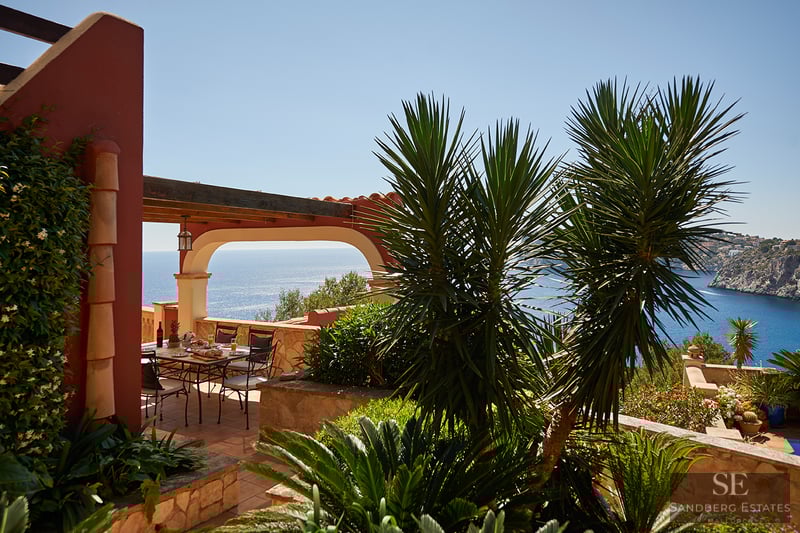 Matplats utomhus på en terrass i terrakotta med bågformad pergola och panoramautsikt över havet.