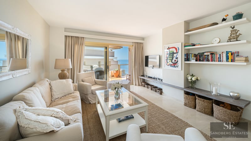 Mediterranean style living room with beige sofas, glass table, and sliding doors opening to a terrace with sea views.