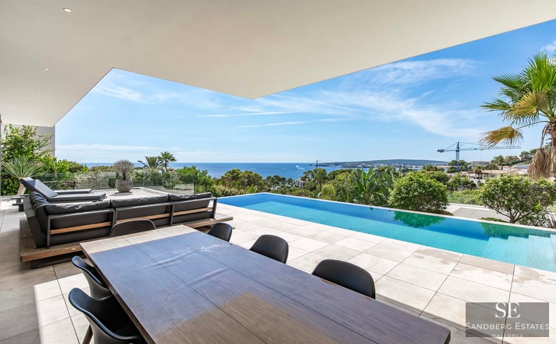 A modern luxury terrace featuring an infinity pool overlooking the ocean, with outdoor dining and lounge seating.